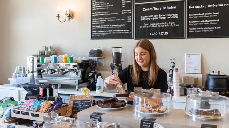 A member of staff serving behind a counter in the café at Dinefwr, Carmarthenshire